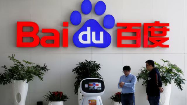 Men interact with a Baidu AI robot near the company logo at its headquarters in Beijing, China April 23, 2021. (File Image: Reuters/Florence Lo)