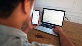F&O Photo shows a person looking at a laptop and a mobile screen with candlesticks showing stock market movement