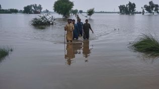 Villagers wade through a flooded area after torrential rains and rising water level in the rivers due to water release from Indian dams, in Pindi Bhattian, Pakistan