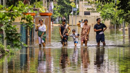 People wade through a waterlogged road after heavy rainfall, at Mithali Nagar, Meerpet, Near Hyderabad, Telangana, Sunday