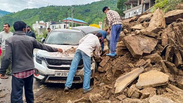 People gather after a vehicle gets stuck under debris as heavy rain triggered landslides and flash floods, in Shimla