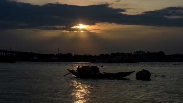 Boatmen row their boats in the Hooghly river near Prinsep Ghat as the sun sets behind clouds, in Kolkata