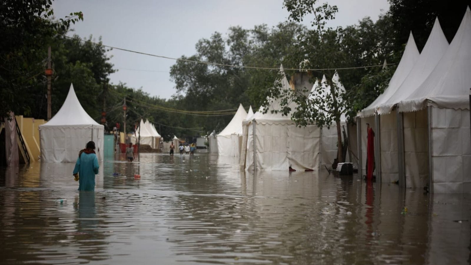 People wade through the leftovers of a relief shelter which was flooded in the Yamuna Bazar in New Delhi on Thursday. Express Photo by Tashi Tobgyal