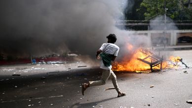 A protester runs next to burning debris from a kiosk outside Bangladesh's national parliament complex in Dhaka, Bangladesh, Friday, Oct. 17, 2025. (AP Photo/Mahmud Hossain Opu)
