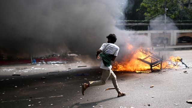 A protester runs next to burning debris from a kiosk outside Bangladesh's national parliament complex in Dhaka, Bangladesh, Friday, Oct. 17, 2025. (AP Photo/Mahmud Hossain Opu)