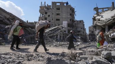 Displaced Palestinians walk with their belongings past destroyed buildings as they return to their homes in Khan Younis, southern Gaza Strip, Friday, Oct. 10, 2025, after Israel and Hamas agreed to a pause in their war and the release of the remaining hostages. (AP Photo/Jehad Alshrafi)