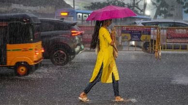 A woman holding an umbrella walks on a road during heavy rainfall in Chennai.