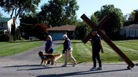 Dan Beazley, of Northville, carries a homemade cross past a therapy dog to The Church of Jesus Christ of Latter-day Saints in Grand Blanc Township, Mich., Tuesday, Sept. 30, 2025, after a man rammed his vehicle into the building before opening fire and setting the building ablaze Sunday morning. (AP Photo/Ryan Sun)