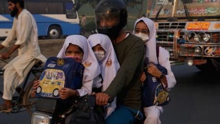 A man with school children wearing masks rides a motorcycle as smog envelopes the area in Lahore, Pakistan, Tuesday, Oct. 28, 2025. (AP Photo/K.M. Chaudary)