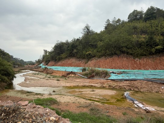 A creek stained orange with mine runoff flows past a rare earth mine near Longnan in south-central China, April 2025