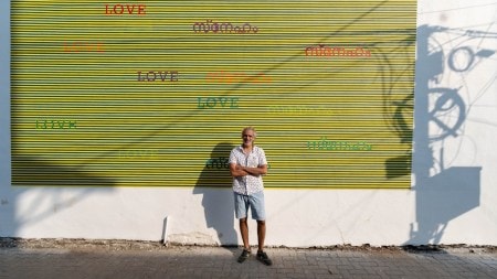 Munir Kabani against the backdrop of his mural on Arthshila wall, Fort Kochi