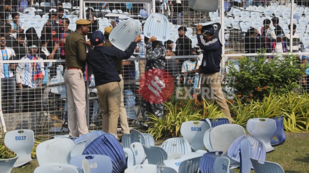 Policemen collect chairs destroyed and thrown by spectators onto the field past the fence. (Express Photo by Partha Paul)