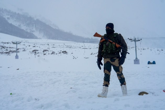 A security official stands guard as tourists visit the snow-laden Kongdori, in Gulmarg, Baramullah district. (PTI Photo)