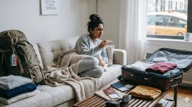 Sick woman on her couch, worried after checking her temperature with packed bags around her