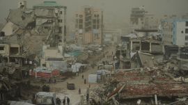 Palestinians walk along a street surrounded by buildings destroyed in Israeli air and ground operations. (File Photo/Representational)