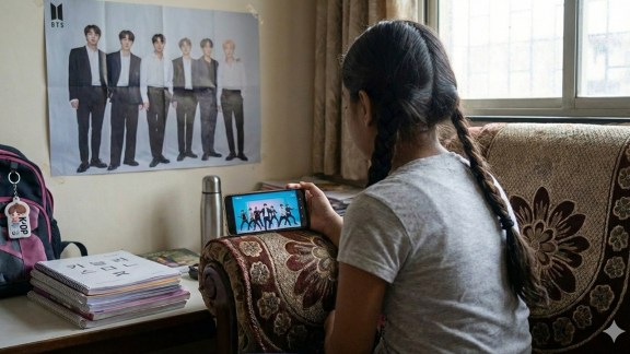 Young girl watching Korean idols dancing on phone screen depicting parasocial bonds