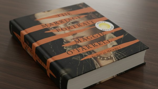 A 3D book cover of Maggie O'Farrell's  <em>The Marriage Portrait</em> lying on a dark brown wooden table 