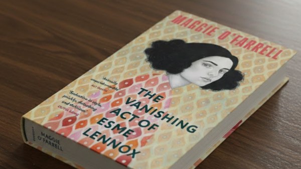 A 3D book cover of Maggie O'Farrell's The Vanishing Act of Esme Lennox lying on a dark brown wooden table 