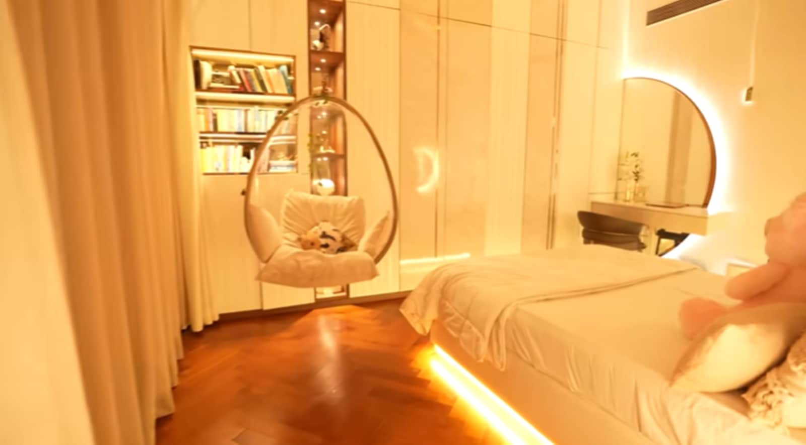 The bedroom continues the home’s soft, rounded aesthetic with curved mirrors, a swing chair by the window and warm lighting under the bed