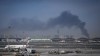 A plume of smoke caused by an Iranian strike is seen in the background as Emirates planes are parked at Dubai International Airport after its closure in Dubai,