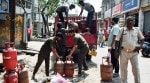 Security personnel stand guard as workers unload petroleum gas (LPG) cylinders