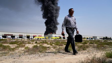 A man walks away after watching a black plume of smoke rising from a warehouse in the industrial area of Sharjah City, United Arab Emirates, Sunday, March 1, 2026, following reports of Iranian strikes in Dubai. (AP Photo)