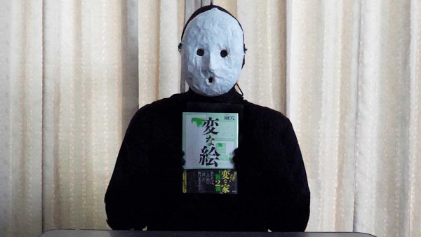 A masked Uketsu stands against a beige background 