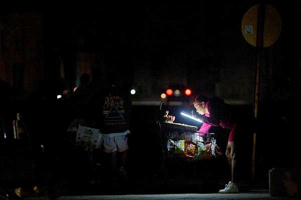 A vendor lights her way with a battery-powered lamp while waiting for customers on the Malecón during a blackout in Havana, Cuba, Saturday, March 21, 2026. (AP Photo/Ramon Espinosa)