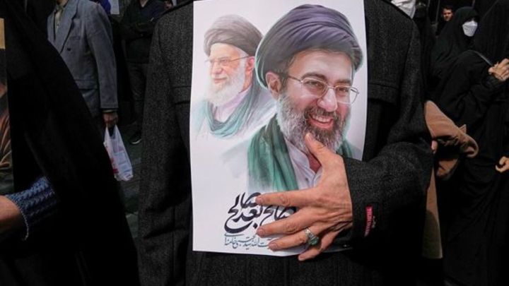 A mourner holds a poster depicting Ayatollah Mojtaba Khamenei, right, the successor to his late father Ayatollah Ali Khamenei, left, as supreme leader, during the funeral procession for senior Iranian military officials and civilians killed during the U.S.-Israel campaign