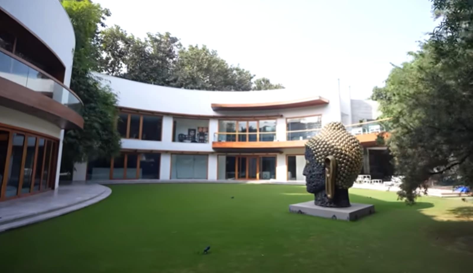 The architecture itself sets the tone, featuring a sweeping curved structure overlooking a manicured lawn, anchored by a towering 25-foot Buddha head sculpture by artist Subodh Gupta.