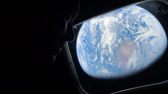 Earth seen through the Orion spacecraft window as an Artemis II crew member looks on during the return journey. (Image: Nasa)
