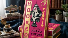 The book cover of Hooked lying on an ornate desk with a sculpture of a fish in the background