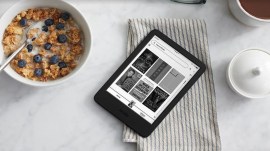 A kindle lies on a table top alongside a bowl of breakfast