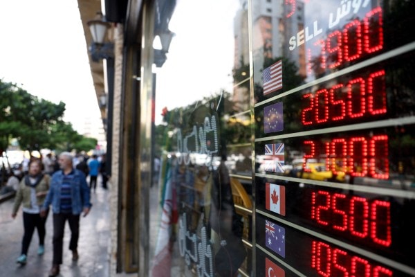 People walk near a display at a currency exchange bureau, as the value of the Iranian rial drops, in Tehran, on May 2, 2026. (REUTERS)