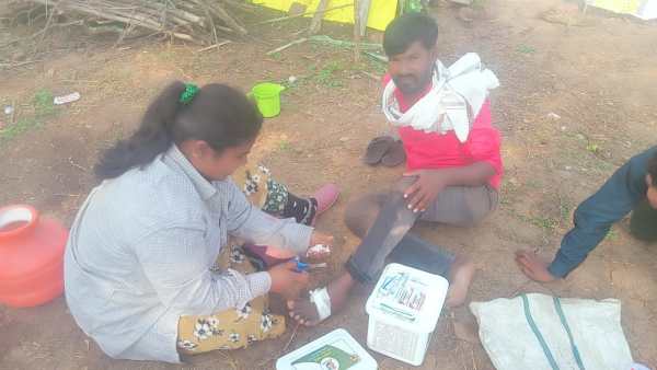 A sugarcane cutter is bandaging the wound of a cane cutter worker in the field.