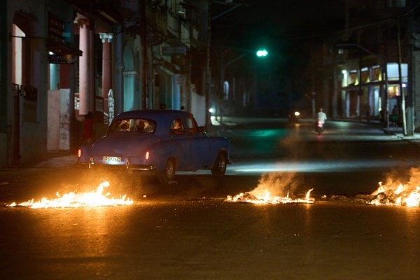 People drive a classic American car through a barricade set up by residents protesting against prolonged power outages in Havana, Cuba. (AP Photo)