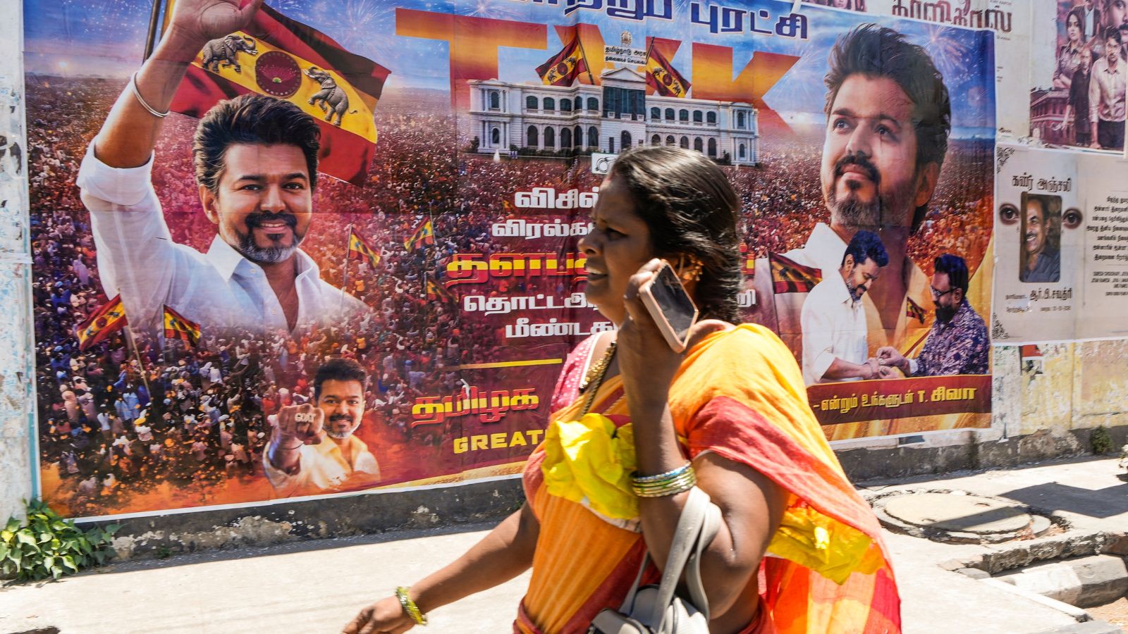 A woman walks past a banner of actor and Tamilaga Vettri Kazhagam (TVK) President Chandrasekaran Joseph Vijay, after his party surprisingly emerged as the single largest party in the April 23 polls to the Tamil Nadu state Assembly. (PTI Photo)