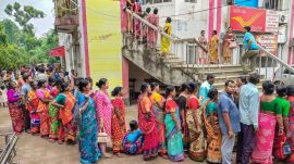 People stand in queue outside a Post Office to complete the verification process for the 'Annapurna Yojana' in West Bengal's Balurghat. (PTI Photo)