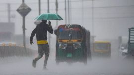 A man carrying an umbrella crosses a road amid rainfall, in Chikkamagaluru, Karnataka. (PTI Photo)