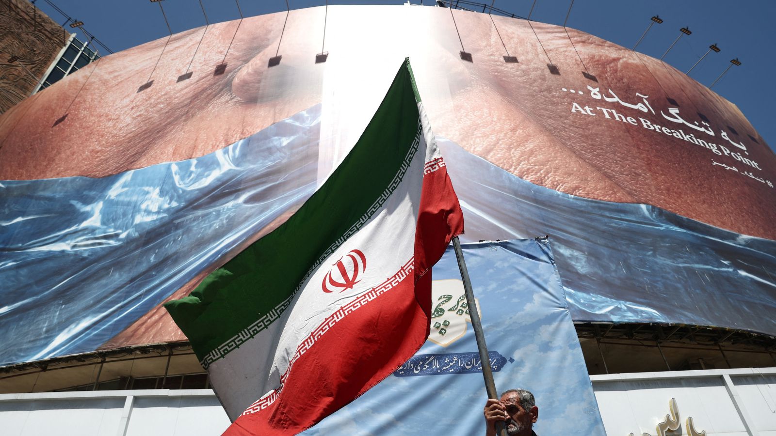 A man holds an Iranian flag near an anti-US billboard depicting US President Donald Trump and the Strait of Hormuz, in Tehran. (REUTERS)