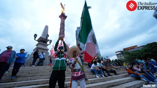 Fans wave a Mexican flag and hold a replica of the FIFA trophy as they gather at the Angel of Independence monument