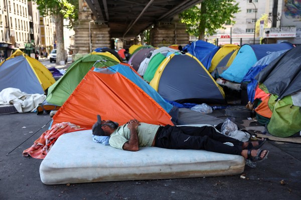 A migrant rests on a mattress near tents at a makeshift camp set up under an elevated railway of a Paris metro line near the Stalingrad subway station, as temperatures rise in paris during a heatwave affecting a large part of France, June 24, 2026. (REUTERS)