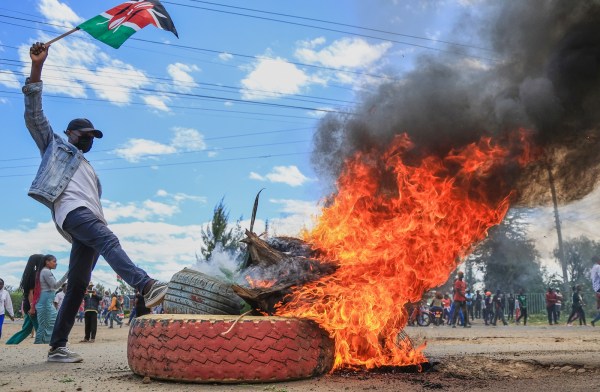 A protester raises a Kenyan flag near a burning barricade during a demonstration against the proposed Ebola quarantine center. (AP Photo)
