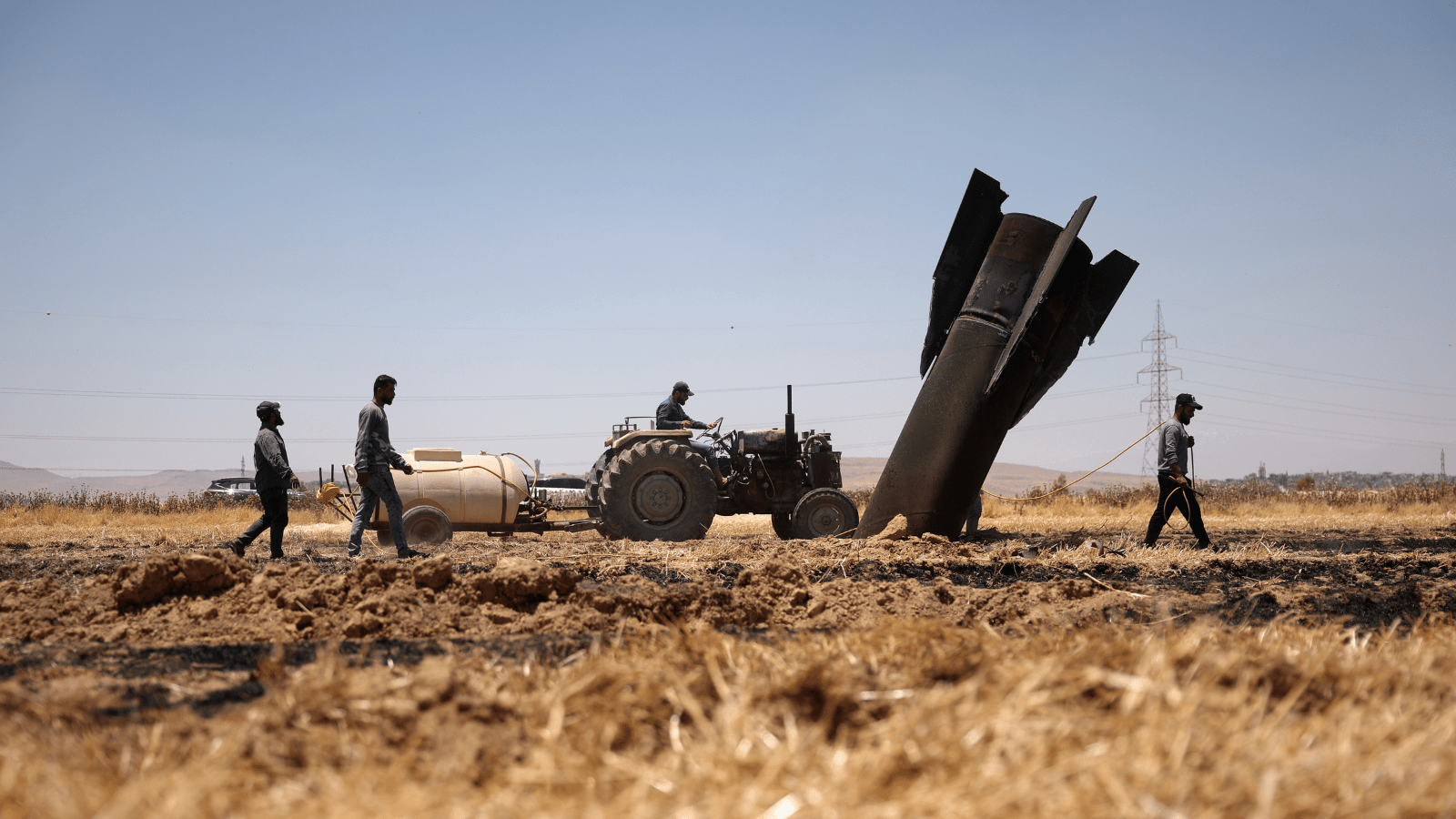 Farmers spray water in a burned agricultural field next to a projectile near the town of Najha, Syria on June 8, 2026, after debris from Iranian missile launches during the Iran-Israel conflict fell in the area. (AP Photo)