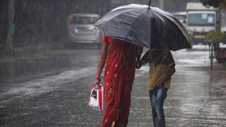 People walk on a road amid rainfall, in Gurugram, Haryana
