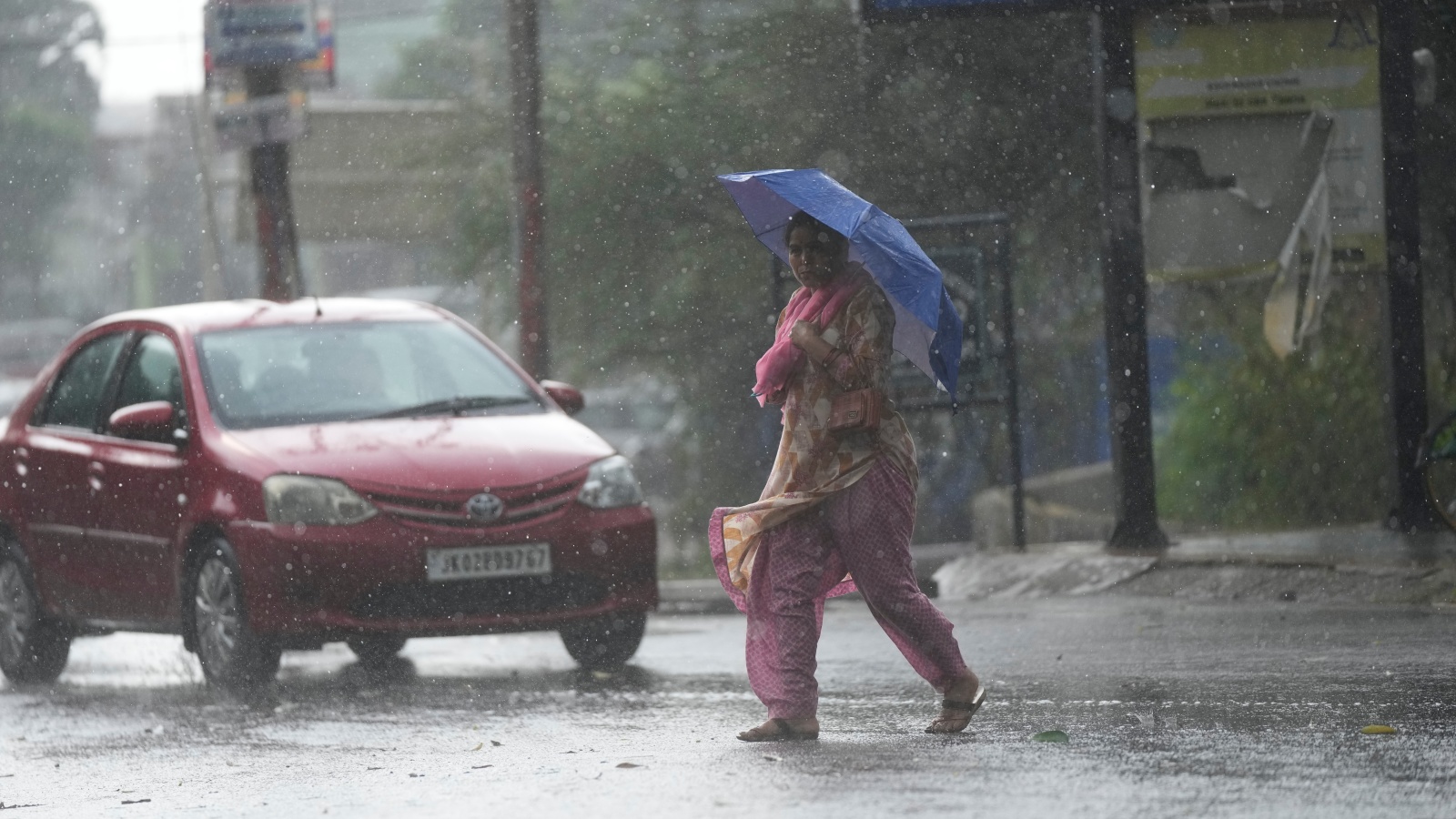 A woman crosses street through a dust storm accompanied by rain in Jammu