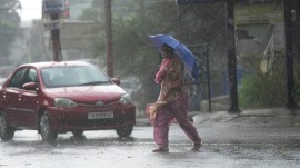 A woman crosses street through a dust storm accompanied by rain in Jammu