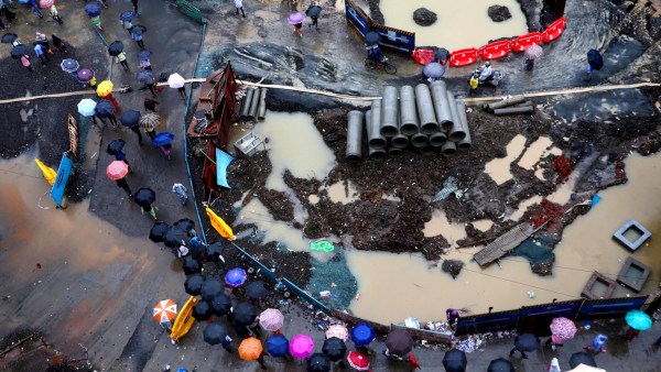 An aerial view shows commuters walking through heavy rain near Prabhadevi railway station as civic construction work continues in Mumbai on Thursday. Waterlogging, potholes, open excavation pits, fallen trees and ongoing infrastructure works continue to pose risks and disrupt daily life during the monsoon.(Express Photo by Akash Patil)