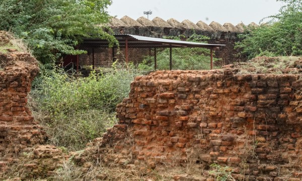 A damaged wall of Indroda Fort with an under construction building in the background.