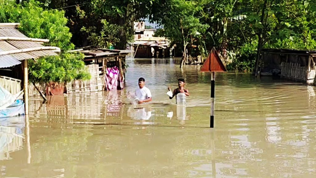 Flood-affected men wade through waist-deep waters carrying household items in a submerged village of Assam's Sivasagar on Tuesday.